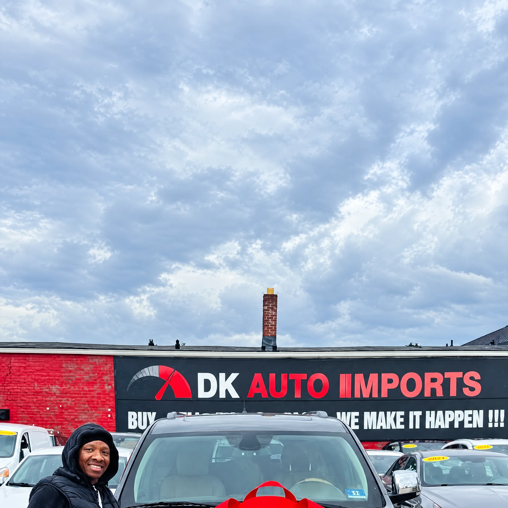 Smiling DK customer in front of the DK Auto Imports sign in Roselle